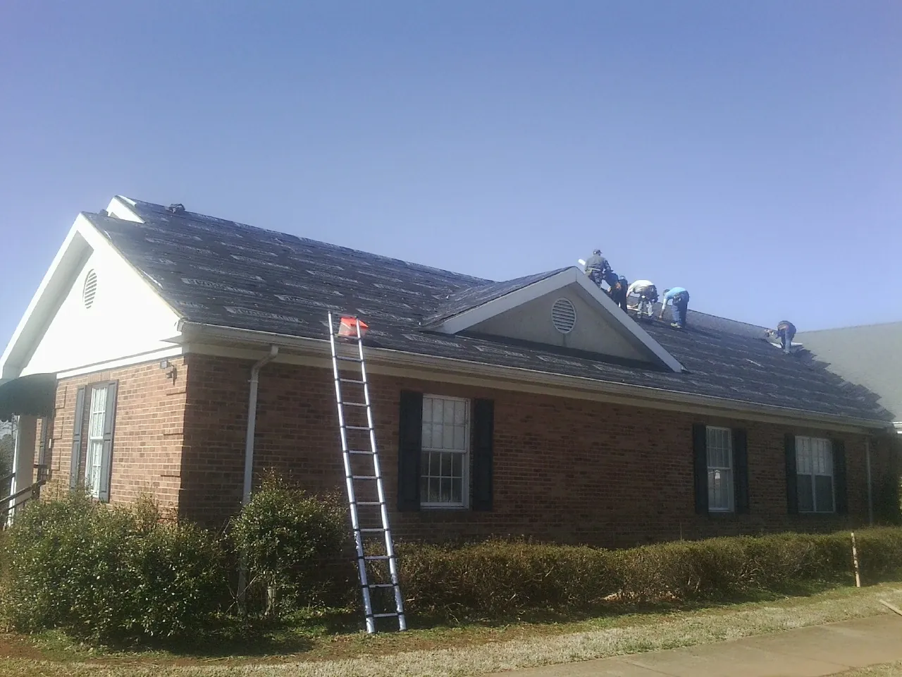 Crew tearing shingles off a brick ranch roof with a ladder set — Metal Roof Repair work by our crew in South Lebanon