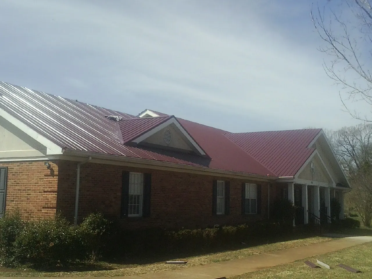 Red metal roof with gabled entries on a long brick building, from a Hail Damage Roof Repair job in South Lebanon