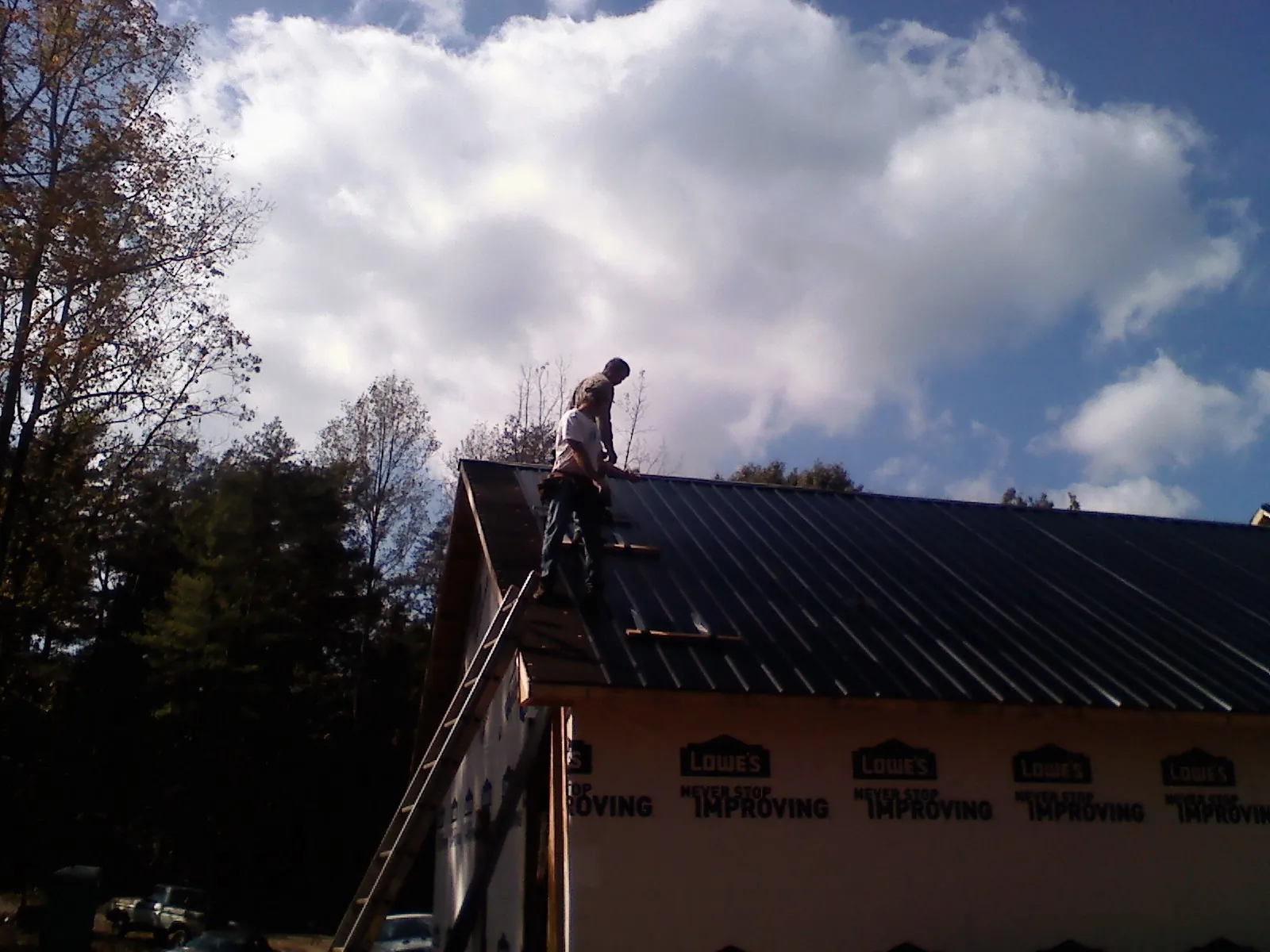 Roofer fastening dark metal panels high against a cloudy sky, from a Roof Inspection job in South Lebanon