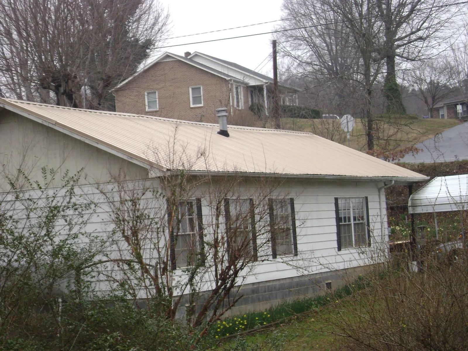 Tan metal roof on a white sided house set into a hillside — Commercial Roofing by Roofing Brothers in South Lebanon